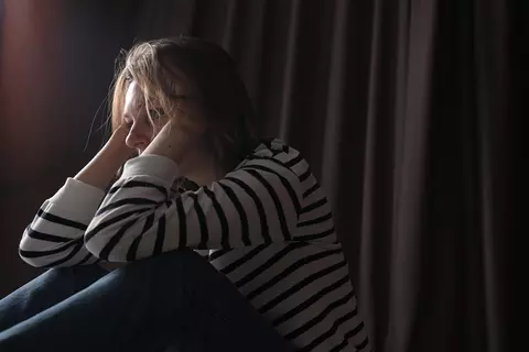 Afbeelding van een vrouw die op de grond zit met haar handen op haar hoofd