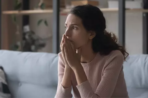 Afbeelding van een vrouw die denkend voor zicht uitkijkt met de handen voor haar mond