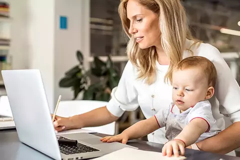 Afbeelding van een vrouw die aan een laptop zit te werken, met een peuter op de schoot