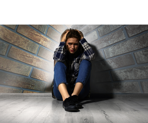 Foto van een vrouw die in een hoek zit, met haar handen op haar hoofd