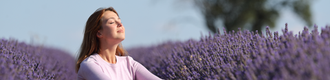 Afbeelding van een vrouw dit in een lavendelveld zit met een glimlach op haar gezicht