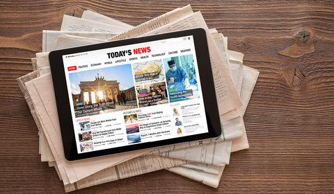 Afbeelding van een tablet met de digitale krant bovenop een stapel papieren kranten
