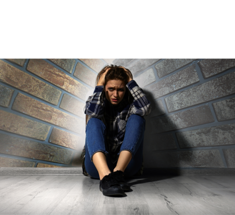 Afbeelding van een vrouw die in een hoek van een kamer zit met haar handen op haar hoofd