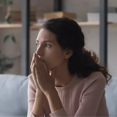 Afbeelding van een vrouw die voor zich uitkijkt met haar handen voor haar mond